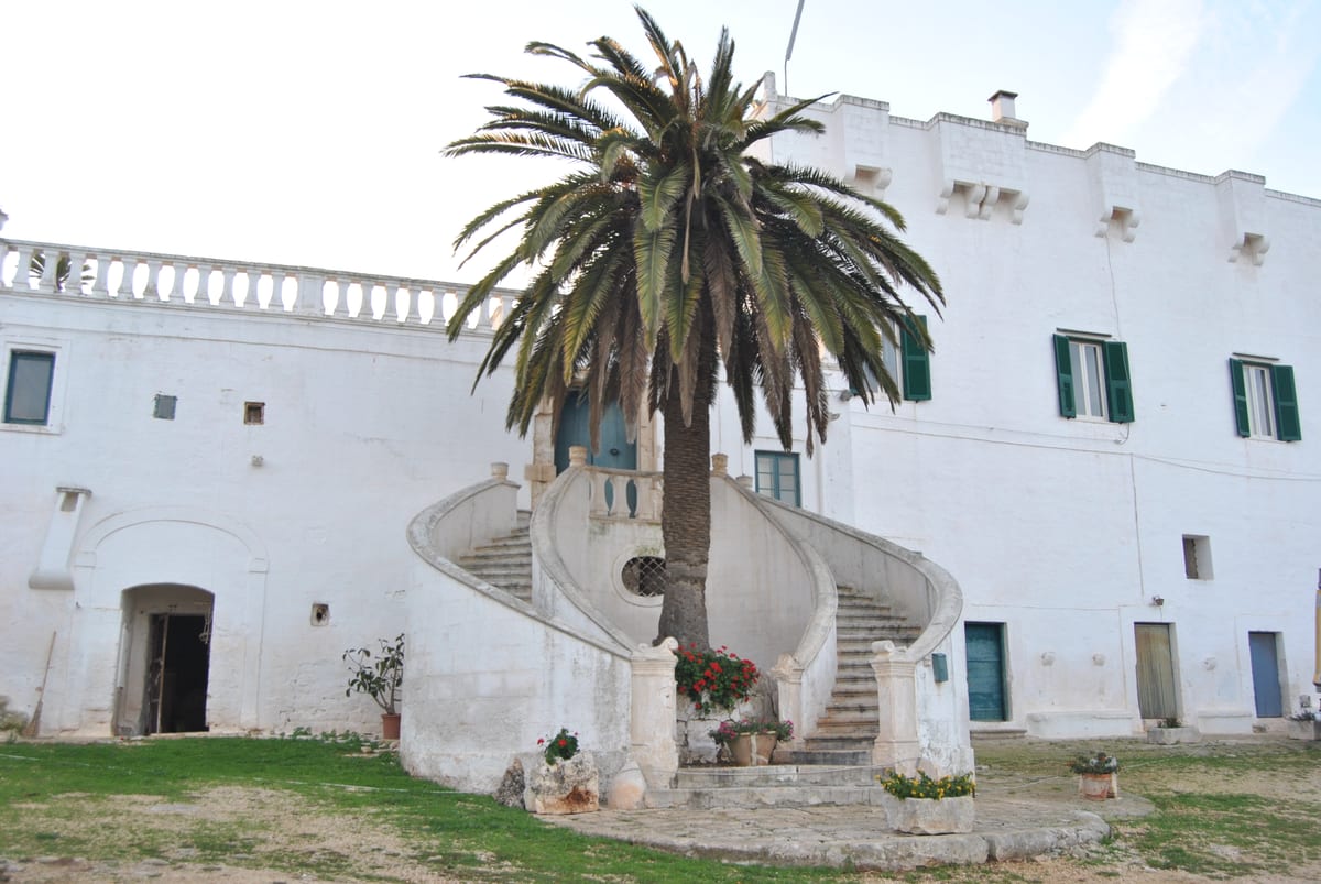 Façade blanche de la masseria Caramanna à Monopoli, avec un escalier double et un palmier